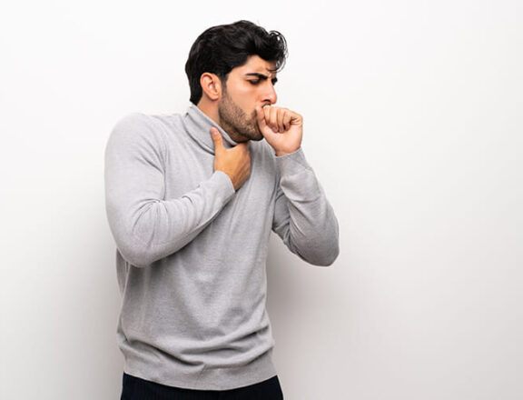 A man clutching his throat with his other hand to his mouth as he coughs